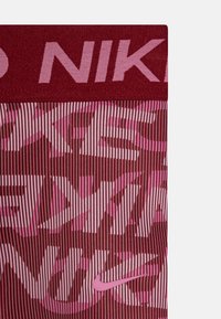 Legginsy Nike z bordowym pasem i różowym paskowanym wzorem z wyraźnym logo. Materiał ma gładkie, teksturowane wykończenie.