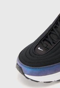 Black sneaker with textured fabric upper, featuring a curved design. Color gradient from black to blue on the sole, with white Nike logo and laces.