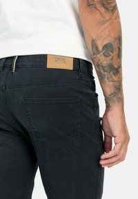 Black denim jeans with a straight cut, featuring a leather patch labeled "camel active" at the waist and back pocket stitching detail.