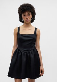 Melnas bezpalodzu kleitas ar kvadrātveida kakla izgriezumu, pieguļošu ķermeni un izplestu svārku. Izgatavota no gludas auduma ar nedaudz spīdīgu tekstūru.