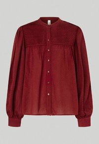 Bordeauxblus med rund krage, knappstängning fram och texturerad övre del. Långa ärmar med elastiska manschetter och en lös passform.