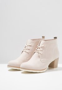 Stivali ankle in suede beige con punta arrotondata, chiusura con lacci e tacco a blocco testurizzato, caratterizzati da un sottile accent metallic sul retro.