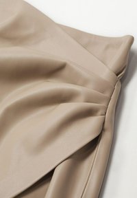 Gonna in ecopelle beige con texture morbida, dotata di dettagli plissettati e una finitura liscia. Il tessuto si drappeggia dolcemente.