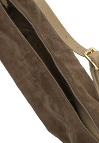 Bruine suède handtas met een beige leren schouderriem en gouden hardware. Beschikt over een met rits afgesloten hoofdcompartiment en een zachte textuur.