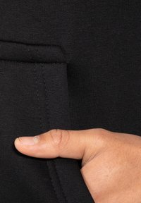 Testo in tessuto nero con una finitura liscia; una mano tiene una tasca alla cucitura, evidenziando la sua funzionalità e design.