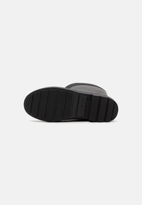 Semelle de botte en caoutchouc noir avec des rainures horizontales et une surface texturée. Présente un léger arc et un design épuré et minimaliste.