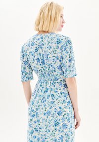 Robe florale en tissu léger présentant des motifs floraux bleus et verts, avec de courtes manches bouffantes, une taille smockée et une silhouette fluide.