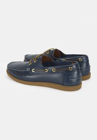 Marineblaue Lederschuhe mit runden Zehen, goldenen Ösen, beigen Schnürsenkeln und einer strukturierten braunen Gummisohle; genähte Akzente an den Seiten.