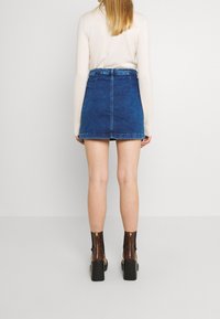 Džínová minisukně v modré barvě s přiléhavým pasem a zadními kapsami. Stylizováno s hnědými platformovými kotníkovými botami a světlým topem.