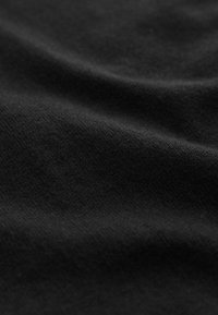 Gros plan sur un tissu noir doux présentant une texture subtile et de légers plis créant des variations de lumière et d'ombre.