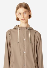 Chaqueta de lluvia ligera en color beige, fabricada con material resistente al agua. Cuenta con capucha, botones a presión plateados y detalles con cordón.
