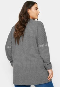 Grå ribbad cardigan med långa ärmar, med en subtil dekorativ kant på ärmarna. Mjuk textur och avslappnad passform, midilengdadesign.