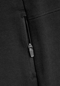 Der schwarze Sweatshirtstoff hat eine mit einem Metallreißverschluss versehene Tasche und eine weiche Textur. Die Nähte sind entlang der Kanten sichtbar.