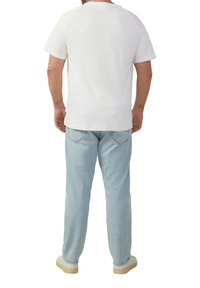 Witte katoenen T-shirt met korte raglanmouwen, gecombineerd met lichtblauwe spijkerbroek en beige sneakers, weergegeven vanuit de achterkant.