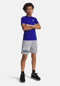 Zils īsām piedurknēm sporta krekls, pelēki šorti ar melno "Under Armour" logotipu, valkāti ar melniem sporta apaviem un tumšām zeķēm. Ikdienas sporta apģērba komplekts.