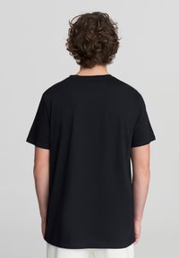 T-shirt nera a maniche corte in cotone. Presenta un colletto rotondo e una vestibilità comoda, con una superficie liscia e senza motivi visibili.