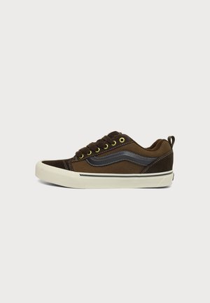 Baskets basses marron avec détail ondulé noir, œillets jaunes, semelle blanche en caoutchouc et languette au talon, vues de profil.
