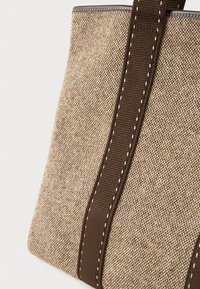 Τσάντα ώμου κατασκευασμένη από υφασμάτινο υλικό σε απαλούς μπεζ και καφέ τόνους, με δύο κάθετες ραμμένες σκούρες καφέ λωρίδες και επίπεδη βάση, σε λευκό φόντο.