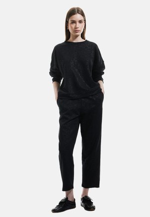 Sort outfit bestående af en langærmet, løs sweatshirt og tapered bukser. Stoffet har en subtil tekstur med glimmer. Sorte sko fuldender looket.