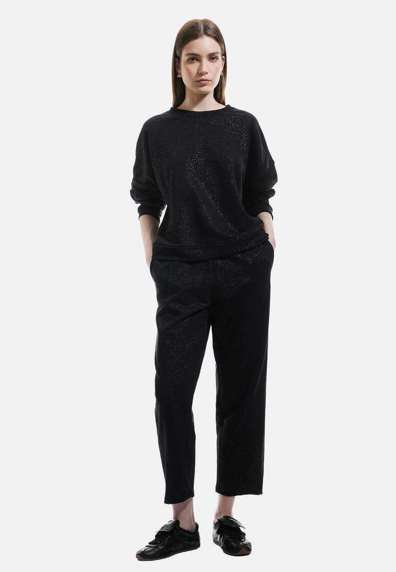 Sort outfit bestående af en langærmet, løs sweatshirt og tapered bukser. Stoffet har en subtil tekstur med glimmer. Sorte sko fuldender looket.