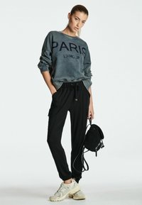 Sudadera gris de gran tamaño con el texto "PARIS L'AMOUR", combinada con pantalones cargo negros ajustados y zapatillas beige. Acentuada con un pequeño bolso negro.