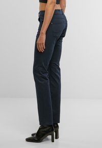 Pantalones oscuros de color azul marino con corte ajustado, la textura de la tela es suave. Presentan bolsillos traseros y detalles de costura sutiles, combinados con botines negros de tacón.