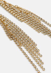 Zelta krāsas pilošās auskaru greznība, kas rotāta ar vairākām rindām caurspīdīgu rhinestone akmeņu, ar elegantu ķēdes dizainu, kas uzsvērti pastiprina to spīdumu.