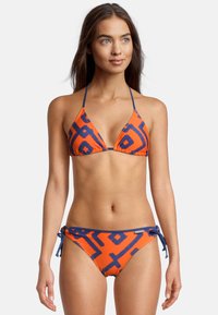 Ensemble de bikini avec un haut triangulaire et un bas à nouer sur les côtés. Orange avec des motifs géométriques bleu marine, fabriqué en tissu lisse et extensible.