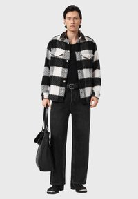 Sort og hvid ternet flannelskjorte, sort t-shirt, løse sorte jeans, sort taske, ankelstøvler med sølvdetaljer, ensfarvet baggrund.