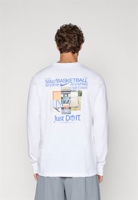 Hvid langærmet t-shirt med grafisk tryk på ryggen, der viser forskellige elementer fra en basketballbane og teksten "Just DO IT." i blå.