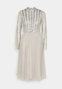 Robe à manches longues en crème avec des sequins argentés disposés en rayures verticales sur le corsage ; jupe fluide et transparente. Design à col montant.