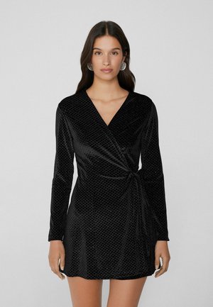 Schwarzes Wickelkleid aus Samt mit langen Ärmeln und einem strukturierten Diamantmuster, das ein seitliches Banddetail als zusätzliches Designelement aufweist.