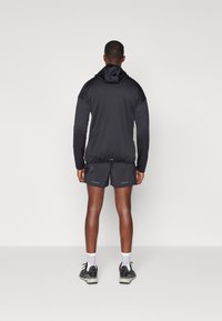 Black hooded jacket with long sleeves, paired with dark shorts. Lightweight fabric, fitted design with reflective accents, and athletic footwear.