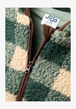 Chaqueta de forro polar a cuadros verde y beige con cremallera marrón; presenta una textura suave y una etiqueta que indica tamaño 12-18 meses.