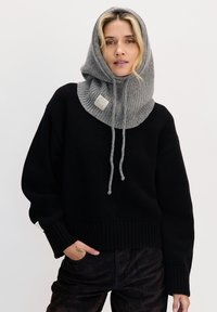 Czarny sweter z dzianiny z szarym prążkowanym kapturem. Kaptur ma sznurki do ściągania i naszywkę z logo. Miękka tekstura i luźny krój.