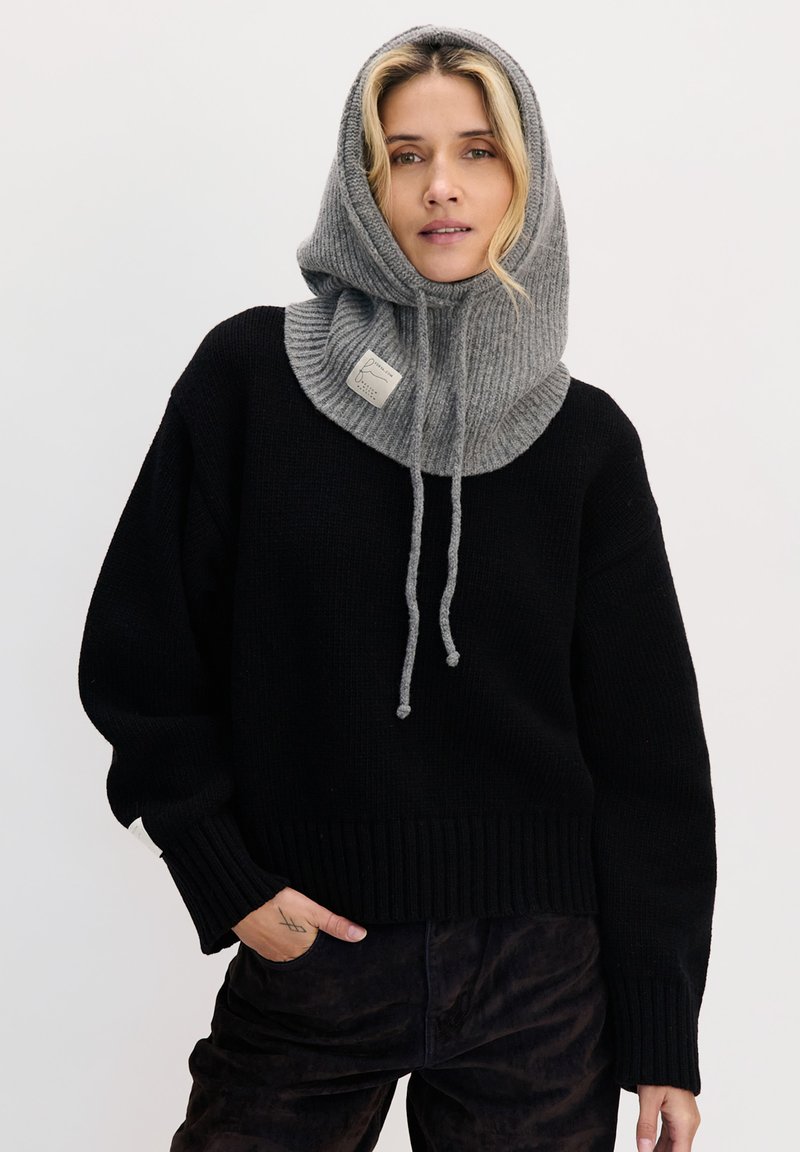 Czarny sweter z dzianiny z szarym prążkowanym kapturem. Kaptur ma sznurki do ściągania i naszywkę z logo. Miękka tekstura i luźny krój.