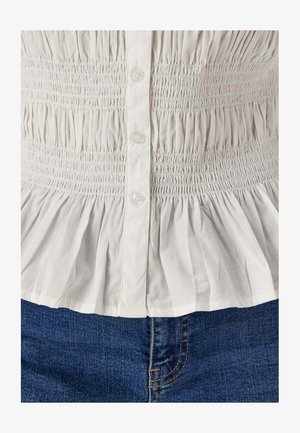 Witte geplooide blouse met knopen gedragen met blauwe spijkerbroek, met gedetailleerde textuur en stofplooien.