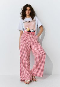 Gray t-shirt with a café print, paired with wide-leg pink and white gingham pants and white flip-flops against a plain background.