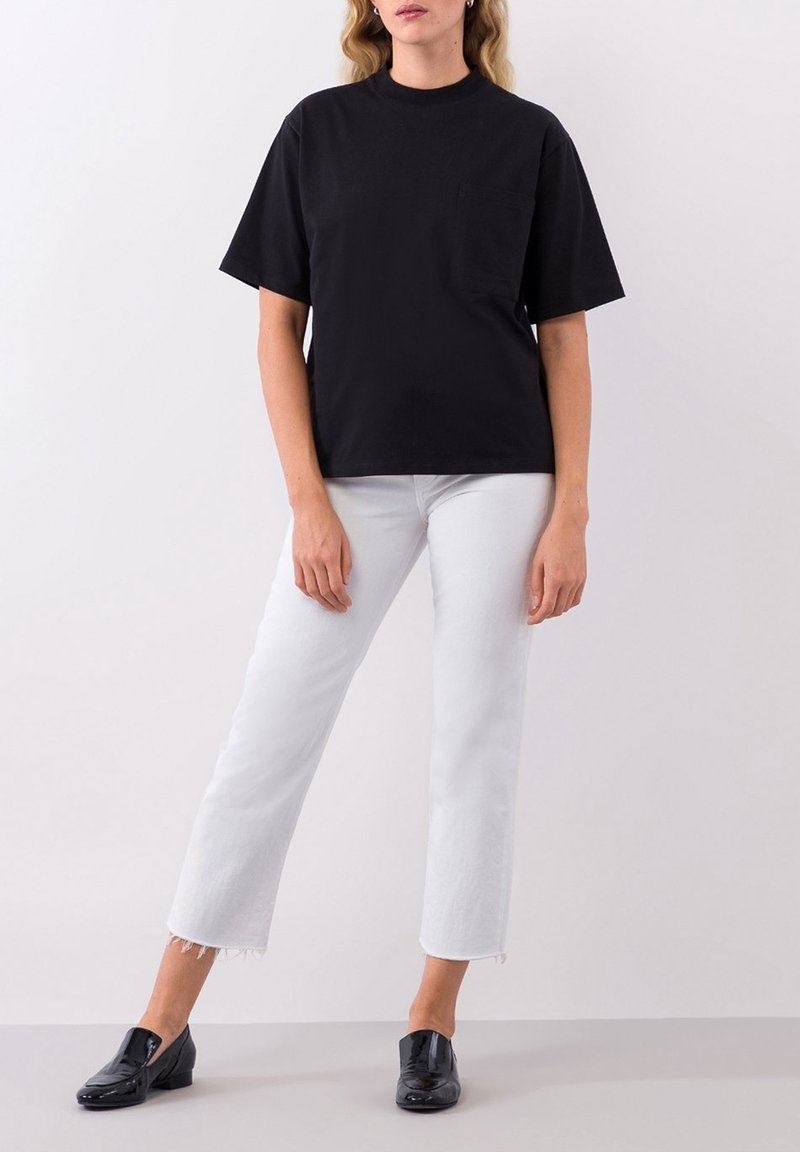 Svart t-shirt med kort ärm, rundad halsringning och bröstficka, matchat med vita croppade jeans och svarta lackloafers.