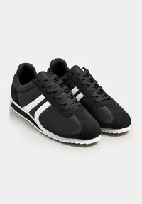 Black athletic shoes with a smooth texture, featuring white stripes on the sides, a lace-up design, and a white outsole.
