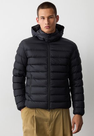Giubbotto imbottito nero con cappuccio, caratterizzato da un design trapuntato, zip frontale e tasche laterali. Texture liscia e silhouette aderente.