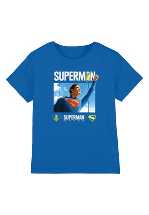 Blue T-shirt with Superman flying upward against a sky background, with "SUPERMAN" text and related logos above and below the image.