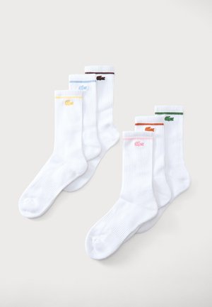 Six chaussettes blanches à bord-côtes, chacune avec un petit logo coloré et une bande assortie près du haut en jaune, bleu, marron, rose, orange et vert.