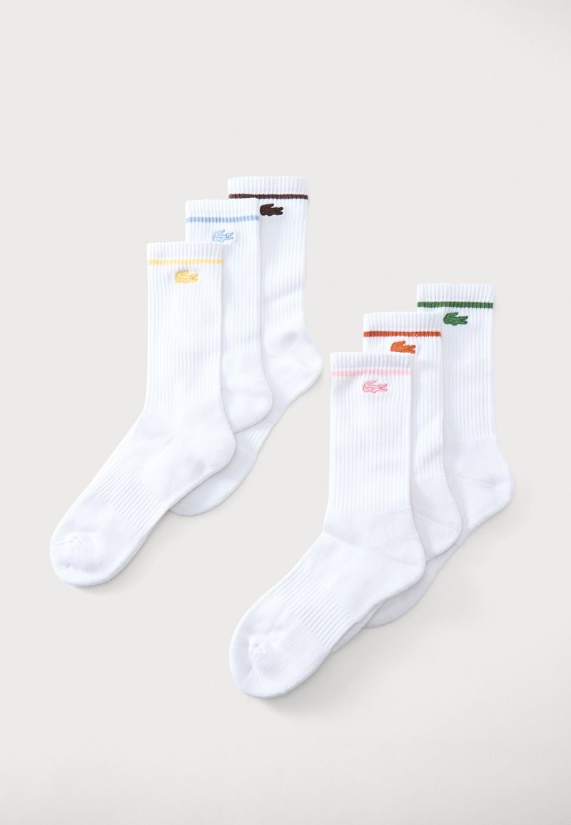Six chaussettes blanches à bord-côtes, chacune avec un petit logo coloré et une bande assortie près du haut en jaune, bleu, marron, rose, orange et vert.