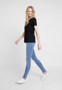Schwarzes T-Shirt mit kurzen Ärmeln in entspannter Passform, kombiniert mit hellblauen Skinny Jeans und weißen Sneakers. Glatte Stoffoberfläche, schlichtes Design.
