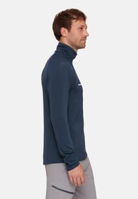 Maglietta a lunga manica blu navy con colletto alto realizzata in un materiale testurizzato. Presenta un piccolo logo sul petto e un design aderente.