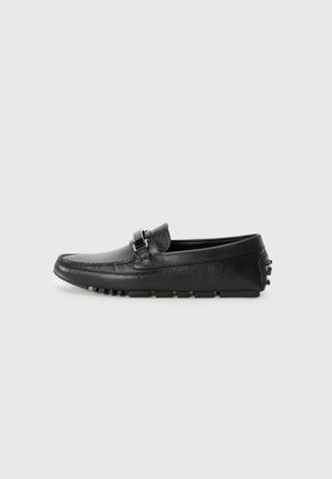 Black leather loafers featuring a textured finish, a decorative buckle, and a rubber sole with protruding accents. Side view displayed.