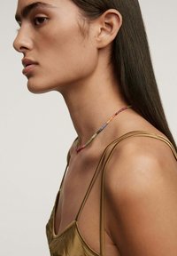 Collar de cuentas colorido con diversas piedras preciosas, usado en el cuello de una persona. Suave, con un ligero brillo; cada cuenta varía en color y tamaño.