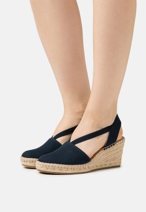 Espadrilles à talon compensé en tissu bleu marine foncé, avec un talon ouvert et un design à sangles croisées ; le talon en jute tressé naturel ajoute de la texture.