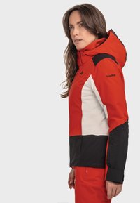 Rote, wei�ße und schwarze Skijacke mit Kapuze, ausgestattet mit einem Farbblockdesign und einem Logo auf der Schulter. Glattes, wetterfestes Material.